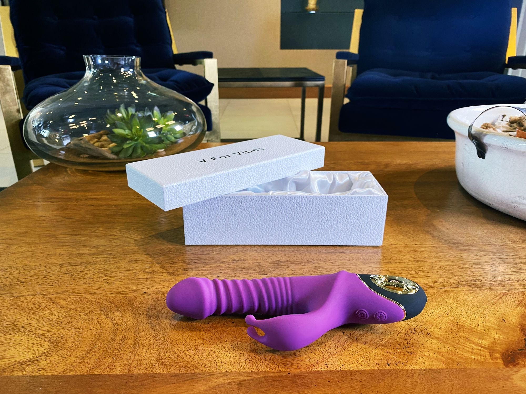 thrusting vibrator for pleasure displayed next to its elegant box on a wooden table in a stylish setting.