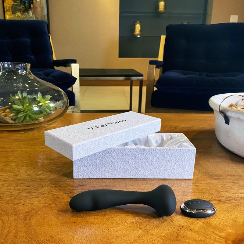 Gaea vibrating black dildo and remote control on a wooden table with luxury decor.